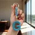 Detailed view of a sparkling blue rhinestone letter G keychain held by hand in bright sunlight. - Letter G