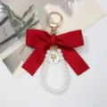 Close-up of elegant large red bow keychain with pearl loop and golden trend charm - Burgundy