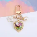 Detailed view of gold heart keychain with pearl and floral charms for bags or AirPods cases. - Fuschia