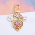 Detail of elegant gold keychain with heart-shaped floral charm and large white pearl. - Peach