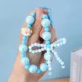 Close-up view of a blue beaded phone charm featuring a delicate hand-made bow detail - Blue