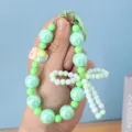 Close-up of green beaded phone strap with a bow and colorful bunny charm details. - Green