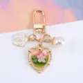 Detailed view of golden heart keychain with pink enamel flower and white pearl charm - Green Pink