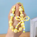 Close-up of yellow beaded bow phone charm with a tiny heart accessory for girls. - Yellow