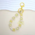 Close-up detail of cute yellow beaded phone strap featuring lucky clover and bow charms - Yellow