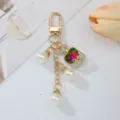 Detailed close-up of perfume bottle charm and imitation pearls on gold-toned keychain - Purple