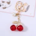 Elegant red acrylic cherry keychain featuring gold metal leaves and a white pearl charm - Transparent Red