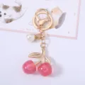 Close-up of pink glittery acrylic cherry keychain with gold metal clasp and pearl - Glitter Pink