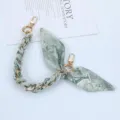 Detailed view of a green patterned silk scarf strap interwoven with a gold metal chain clasp. - Style Y
