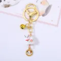 Detail shot of a cute white ceramic cat keychain with a golden bell and charm - Dog