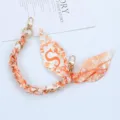 Close-up of orange patterned silk scarf phone strap with letter S and gold clasps - Style S