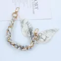 Close-up detail of a braided gold chain and silk scarf phone strap with H pattern - Style H