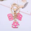 Close-up of pink enamel camera and heart charms on a gold-toned keychain - Camera Style / XO Decor / Pink