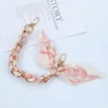Macro view of pink floral silk scarf interwoven with elegant gold metal phone chain - Style X