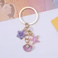 Detailed close-up of purple shell, pink starfish and flower charms on a gold keychain - Purple