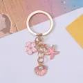 Detail view of gold-tone keychain with pink enamel starfish, flower, and pearl shell charms - Pink