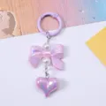 Close-up of a candy-colored bow and heart keychain pendant with iridescent finish details - Purple