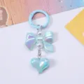 Detail view of an iridescent light blue bow and heart-shaped bag charm with pearls. - Blue