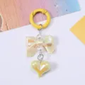 Close-up of cute pearlescent heart and bow charm keychain with yellow spring hook - Yellow
