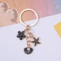 Elegant black enamel shell and starfish keychain with pearl accent in gold finish. - Black