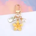 Dettaglio di un portachiavi in lega dorata con ciondolo a fiore di ciliegio e perla. - Giallo