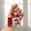 Main tenant des porte-clés étincelants en strass lettre F en rouge, argent et rose - Style F / Rose