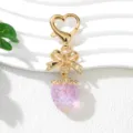 Close-up of cute pink UV strawberry keychain with gold bow and heart clasp - UV Purple