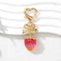 Detail shot of a UV plated strawberry keychain with golden bow and heart-shaped clasp - Iridescent Red