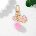 Close-up detail of a pink cherry blossom keychain with fluffy pom-pom and gold hardware - Pink
