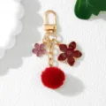 Close-up of elegant gold keychain with red pom-pom and enamel cherry blossom flower charms - Burgundy