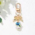Detailed macro shot of gold bow keychain featuring blue flower and large clear crystal - Lake Blue