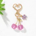 Close-up of a glittering pink resin cherry keychain with gold heart clasp and flower charm - Purple