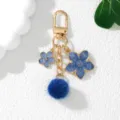 Blue floral keychain with cherry blossom charms and soft pom-pom detail on white surface - Sapphire Blue