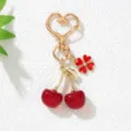 Detailed close-up of red resin cherry keychain featuring a gold heart-shaped metal clasp. - Red
