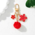 Detailed view of a red cherry blossom and pom-pom keychain with gold-tone hardware - Red