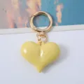 Close-up of a glossy yellow heart-shaped acrylic keychain with a gold carabiner clasp. - Yellow