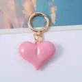 Close-up of a glossy pink acrylic heart-shaped keychain with a polished gold ring. - Pink