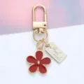 Close-up detail of a red enamel flower keychain featuring a silver Hand made tag - Daisy Pendant (With Hand Made Tag) / Burgundy