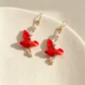 Macro detail of elegant red ceramic bird earrings featuring delicate white pearls - Red