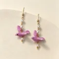 Close-up detail of purple ceramic bird and pearl tassels on stylish drop earrings - Purple