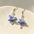 Detailed macro shot of blue ceramic pigeon earrings with pearls and golden hooks - Blue