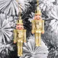Detail von zwei goldfarbenen Nussknacker-Soldaten-Ornamenten an einem verschneiten Baum. - 2er-Set (12*4*2.5cm) / Gold