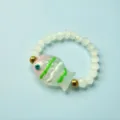 Detailed shot of a colorful glass fish charm on a white faceted bead elastic ring - White