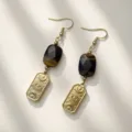 Macro detail of vintage gold earrings with moon eye motif and dark natural stone. - Tiger's Eye