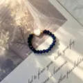 Macro detail of a navy blue crystal beaded elastic ring with a white shell heart charm - Stretch / Black