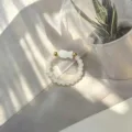 Detail view of a handmade elastic ring featuring white beads and a shell fish charm. - Shell Fish (Stretch) / White