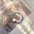 Close-up view of a light blue beaded elastic ring featuring a white shell heart charm. - Stretch / Lake Blue
