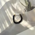 Close-up of a handmade elastic ring featuring a white shell fish charm and faceted black beads - Shell Fish (Stretch) / Black