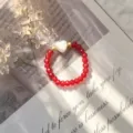 Close-up of a red crystal beaded ring featuring a white shell heart and golden accents. - Stretch / Red