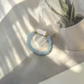 Detailed macro shot of handmade elastic ring with blue frosted beads and white shell fish - Shell Fish (Stretch) / Lake Blue